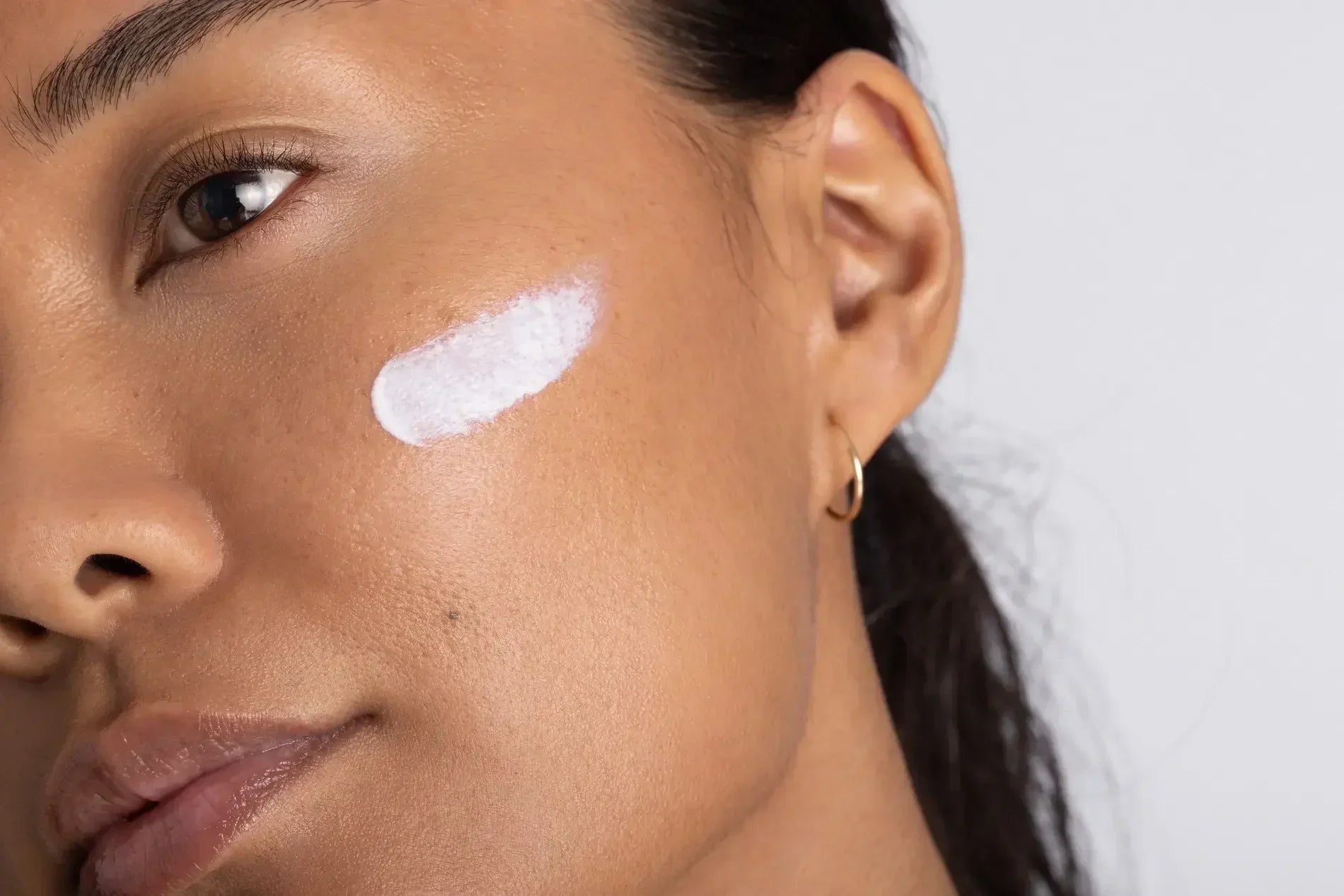 Close-up profile of a woman with a swipe of white cream on her cheek, illustrating how much sunscreen to apply to the face.