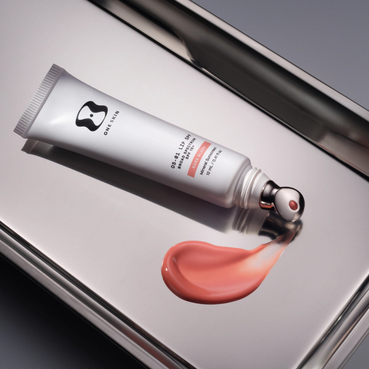 Lip balm tube with a swatch of pink lip balm on a metallic surface