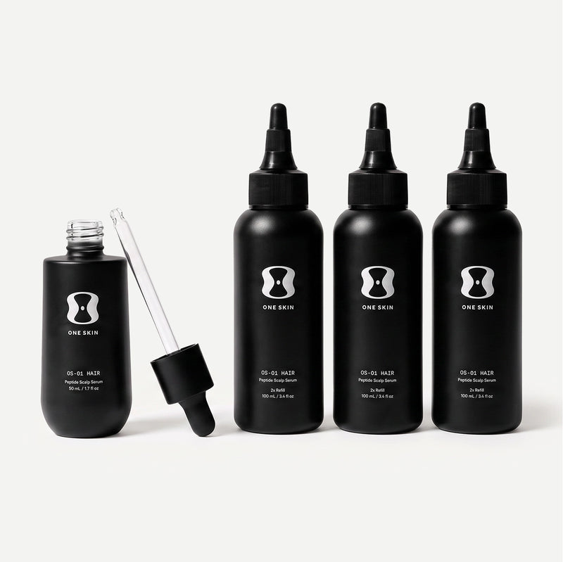 Set of black hair serum bottles with dropper on a light beige background. Contains descriptive text stating Bottle size may vary. The 6-month supply will always come with 150mL of the OS-01 HAIR serum.