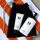 Two skincare products from 'ONE SKIN' on a black drawstring bag with an orange and white striped towel in the background.