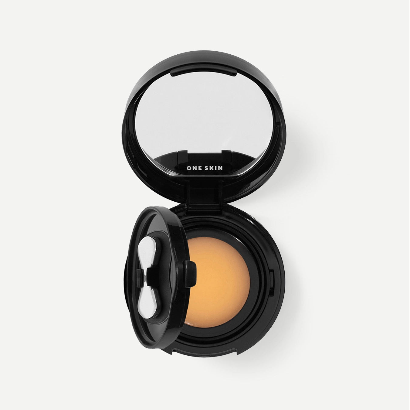 An open black One Skin cushion foundation compact, showing the warm beige foundation powder and the built-in mirror inside the lid, set against a clean off-white background.