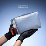 A metallic silver cosmetic pouch held by two hands wearing black gloves, with a blue gradient background and text overlay highlighting water-resistant construction.