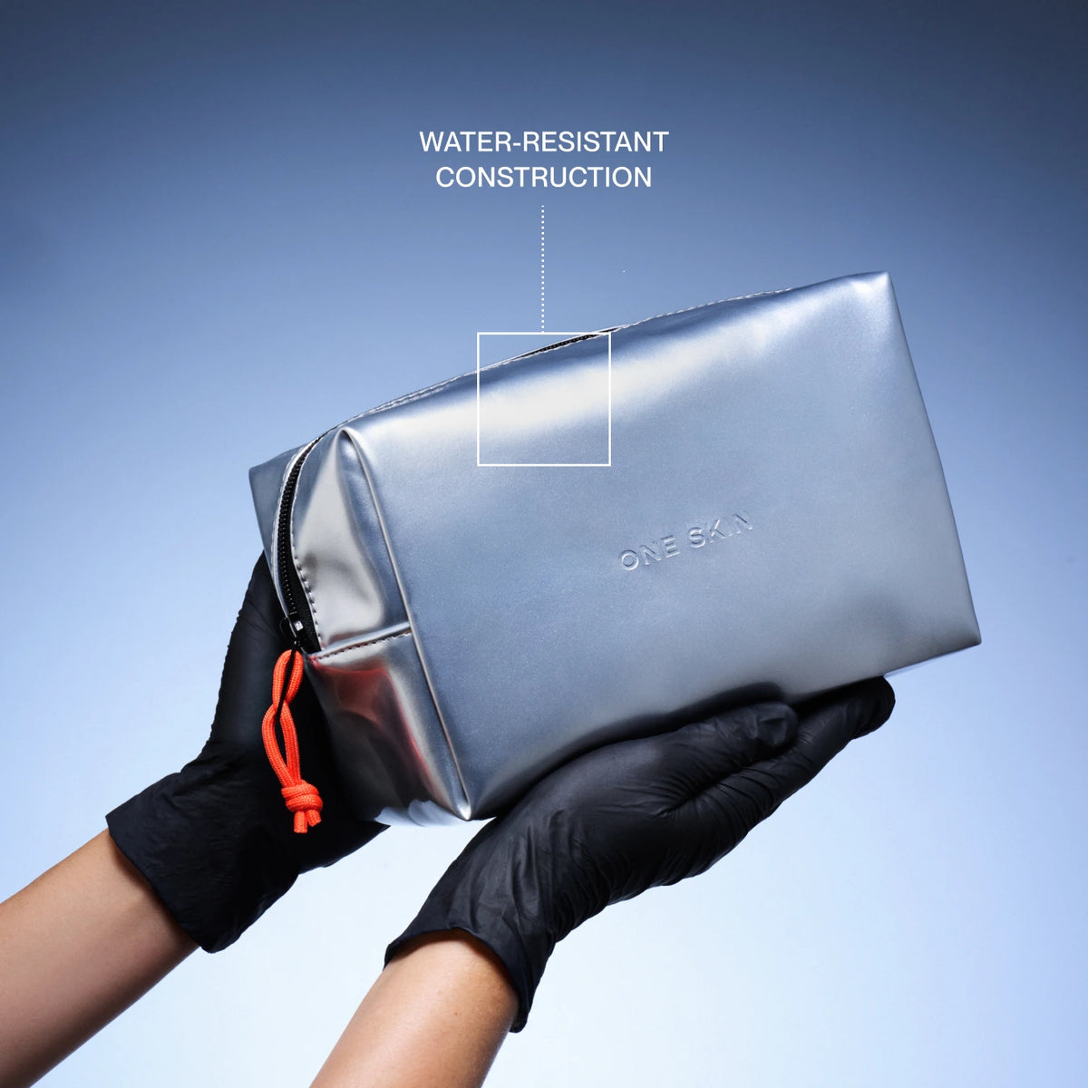 A metallic silver cosmetic pouch held by two hands wearing black gloves, with a blue gradient background and text overlay highlighting water-resistant construction.