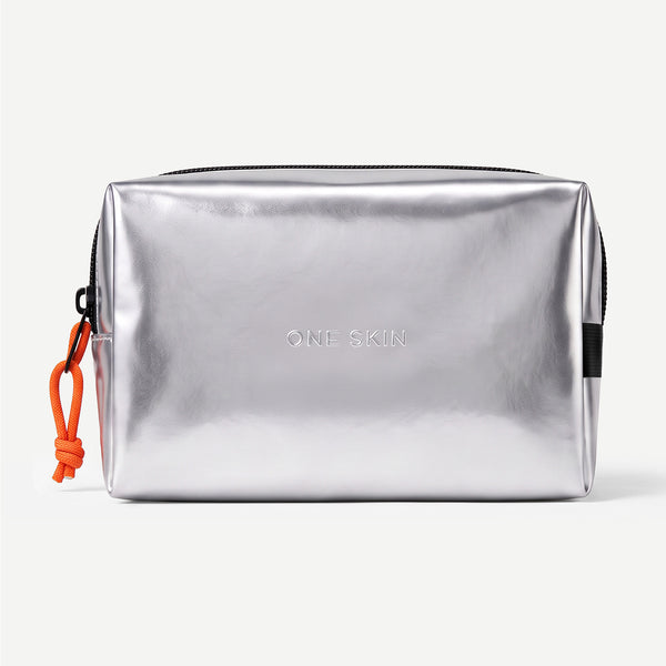 A metallic silver cosmetic pouch with a black zipper, featuring the debossed brand name 'ONE SKIN' in the center and an orange drawstring tag on the left side, set against a plain light gray background.