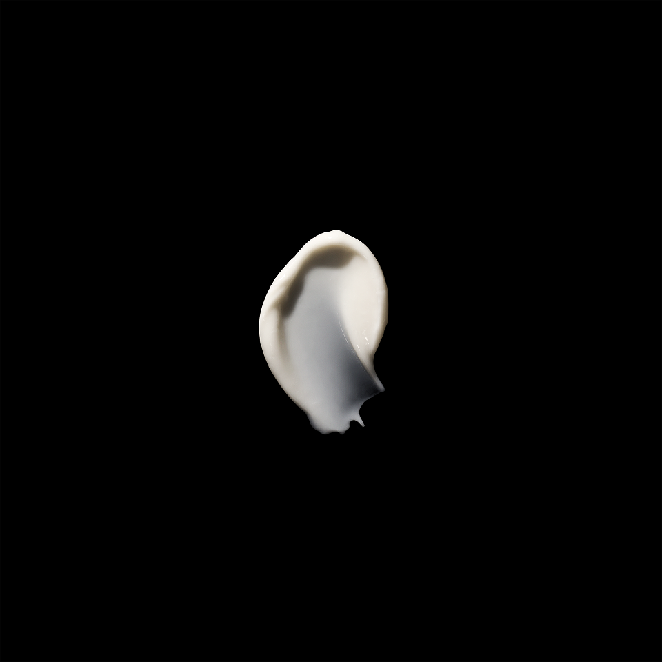 A thick, creamy white swatch of cosmetic cream or lotion on a solid black background.
