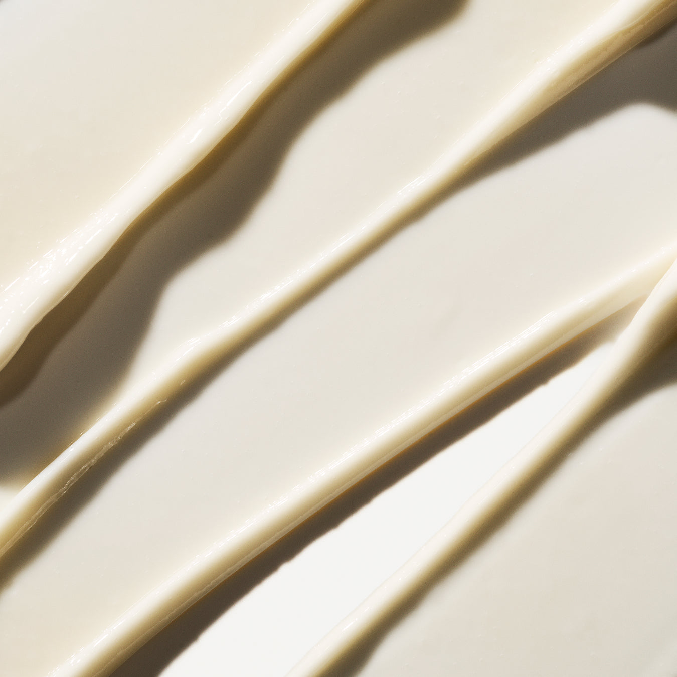 A close-up of a thick, creamy off-white cosmetic product swirled in diagonal streaks with soft shadows.