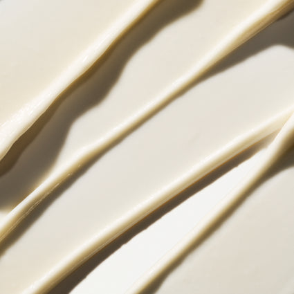 A close-up of a thick, creamy off-white cosmetic product swirled in diagonal streaks with soft shadows.