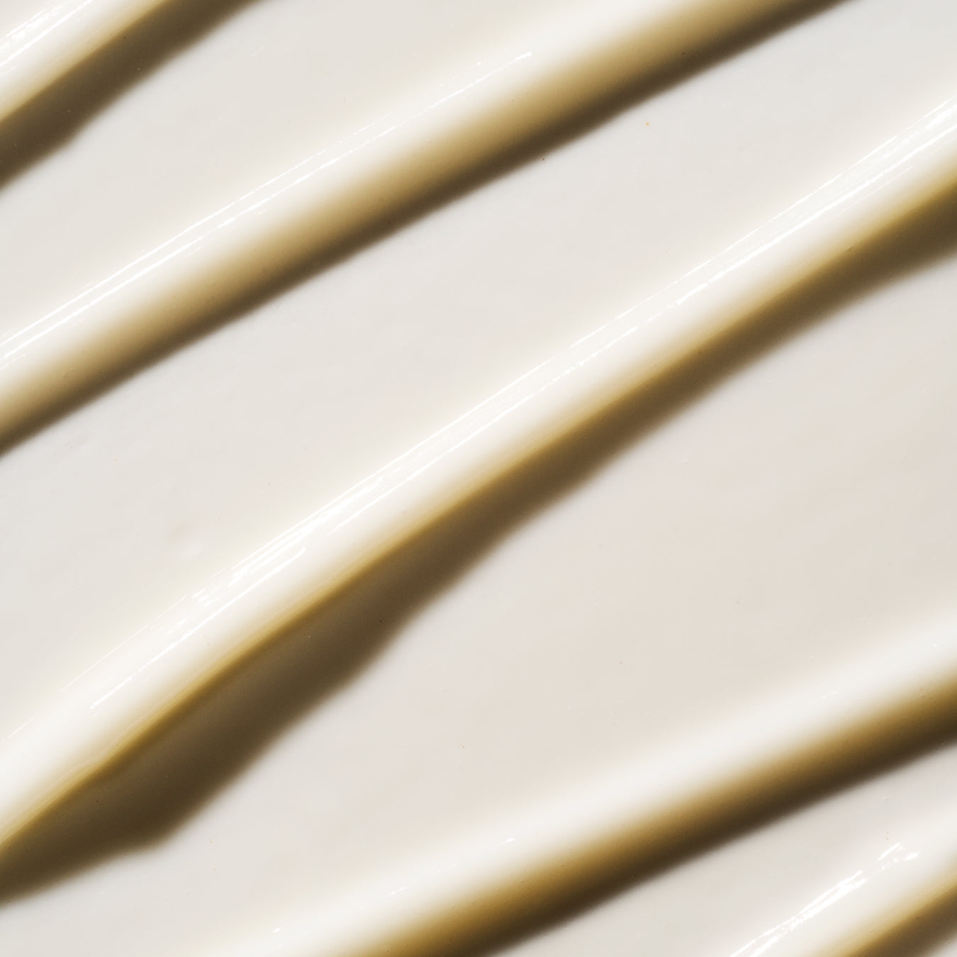 A close-up texture shot of a thick, creamy off-white cosmetic product, swirled in diagonal strokes with soft shadows.