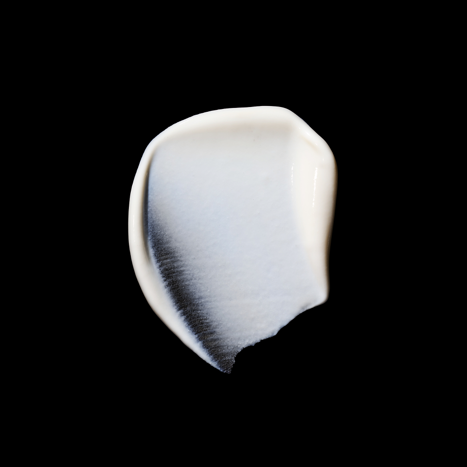 A thick, creamy white cosmetic swatch with a glossy finish, showing a gradient from white to a soft gray edge, set against a solid black background.