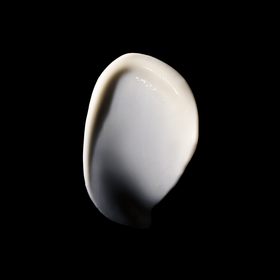 A thick, creamy white swatch of cosmetic cream or lotion on a solid black background.