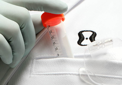 A close-up of a white medical scrub or fabric surface with a small black-and-white ONE SKIN logo and a gloved hand holding a clear vial with an orange cap.