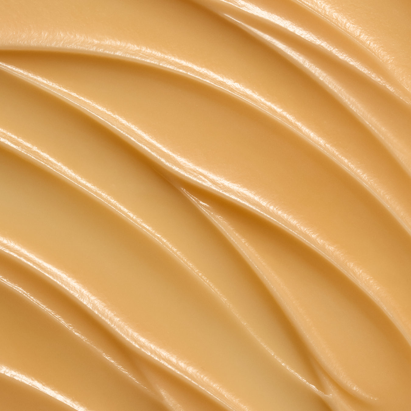 A close-up texture shot of a smooth, creamy beige cosmetic cream with elegant diagonal ridges and soft highlights.