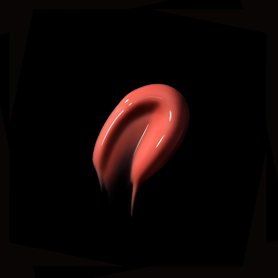 A glossy, smooth swipe of coral pink cosmetic cream or lip gloss on a solid black background.