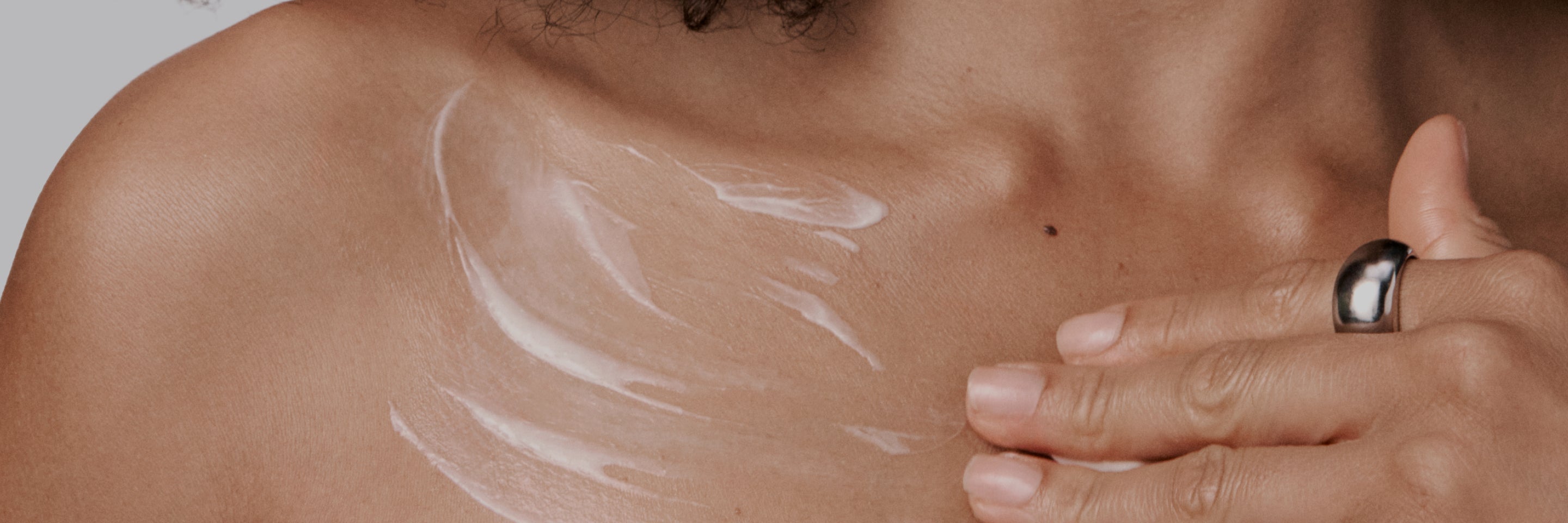 Close-up of a hand applying white cream to a shoulder