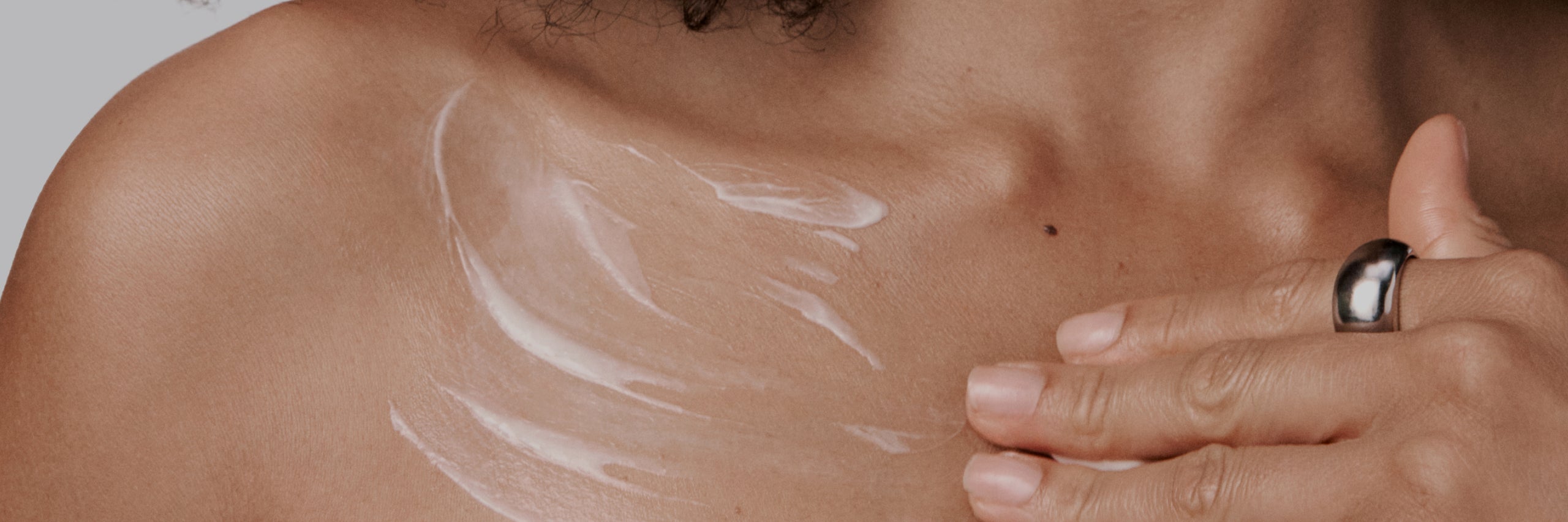 Close-up of a hand applying white cream to a shoulder