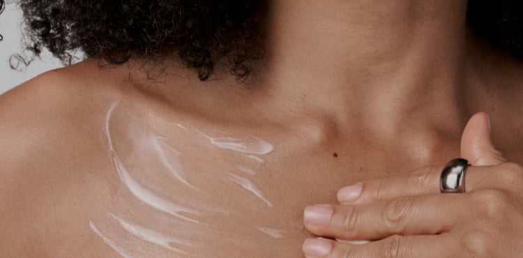 Close-up of a person applying a white cream or lotion to their shoulder.