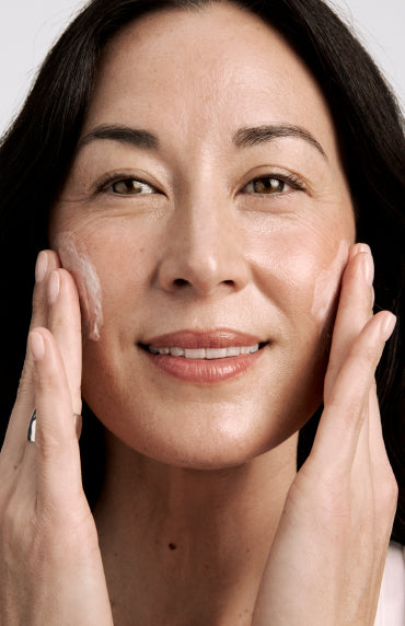 Woman applying cream to her face with a neutral background