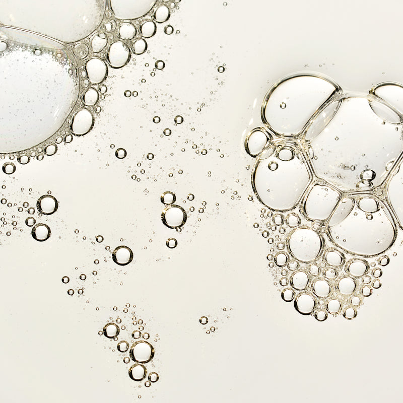 Close-up of clear, transparent bubbles with thin rims floating on a very light warm off-white background.