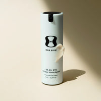 White cylindrical container with black lid labeled 'One Skin' on a beige background