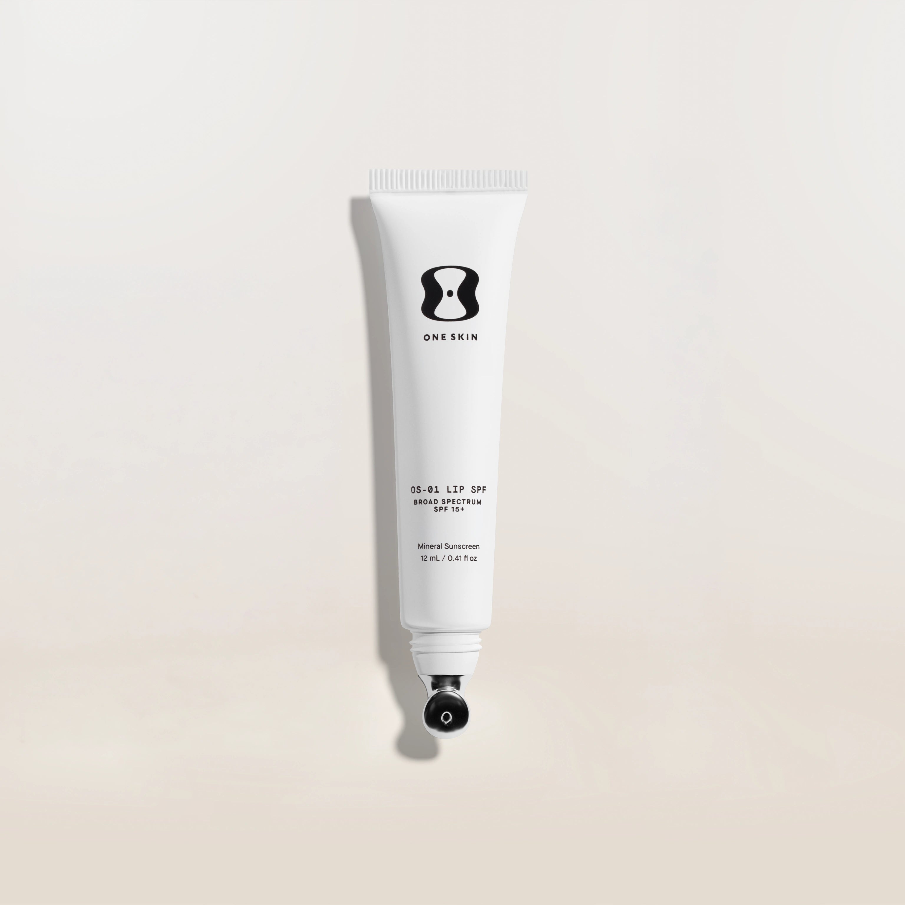 White tube of One Skin lip spf on a light beige background