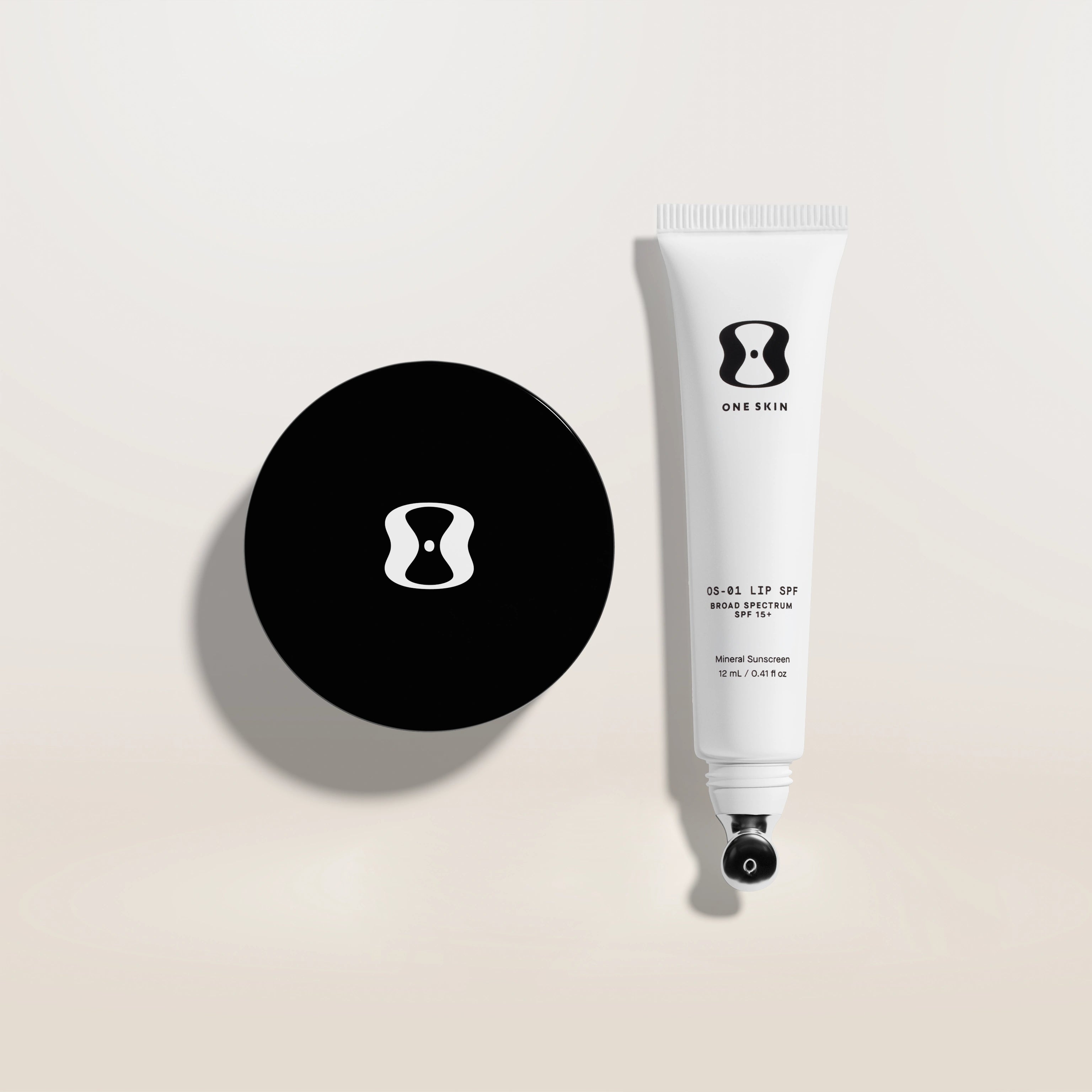 Black round compact and white tube with brand logo on a beige background