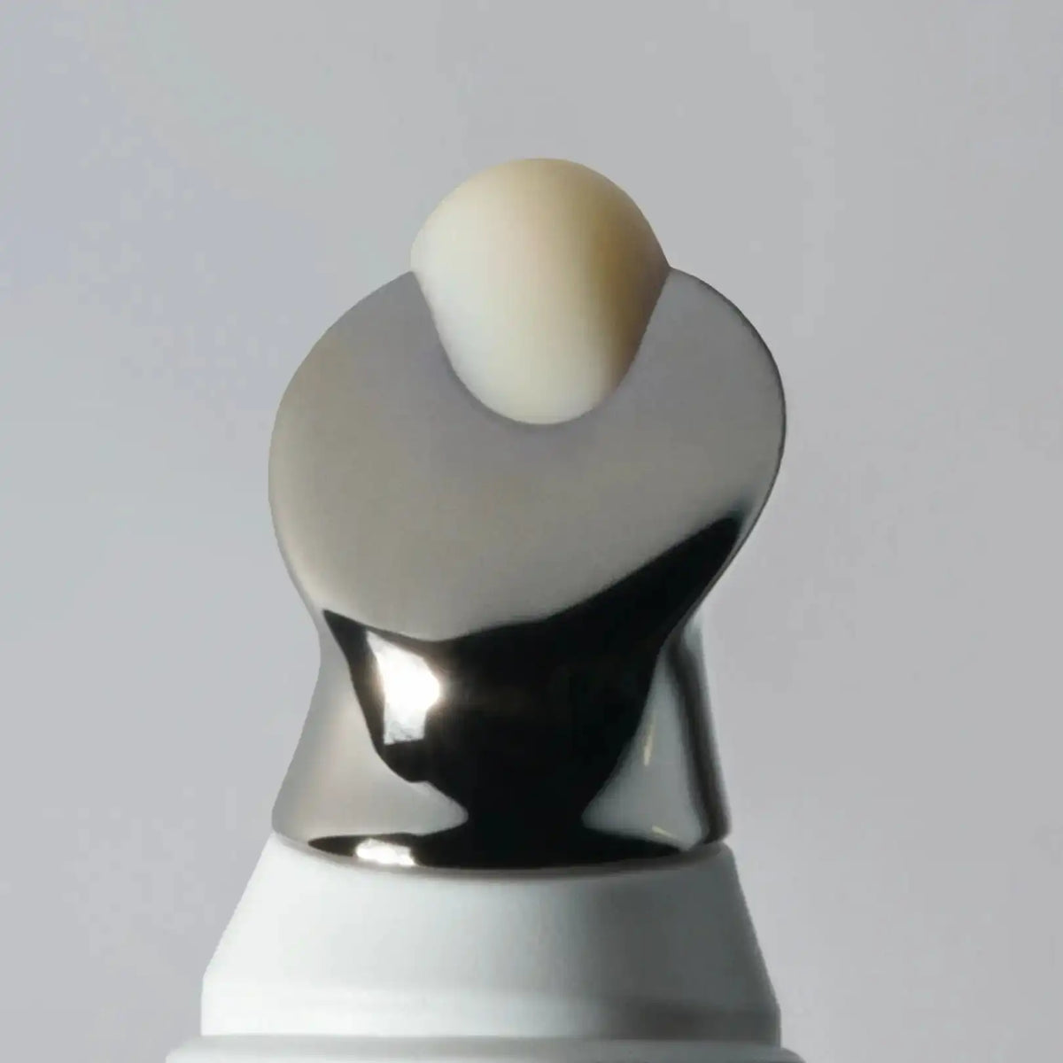 Sculptural object with a spherical beige top and metallic silver base on a gray background
